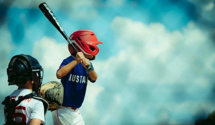 Youth baseball batter at the plate under a bright blue sky